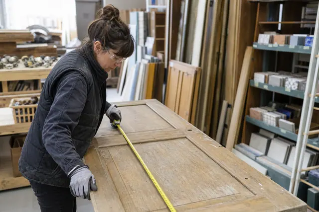 Bricoleuse mesurant une porte en bois dans une ressourcerie de matériaux.