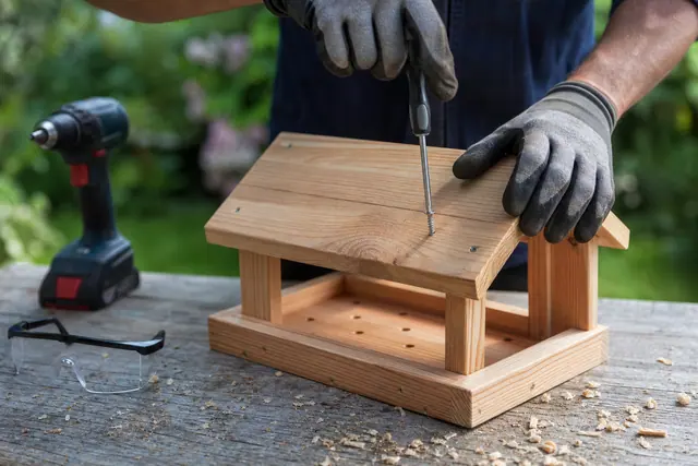Montage d’une mangeoire en bois à toit incliné sur un établi de jardin.