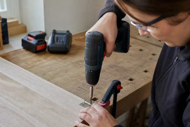 Perceuse-visseuse compacte utilisée avec lunettes sur un panneau de bois fixé.
