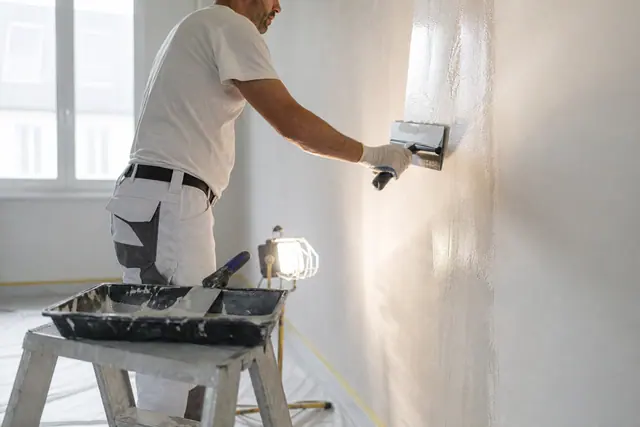 Applicateur passant un enduit de lissage au couteau large sur un mur intérieur