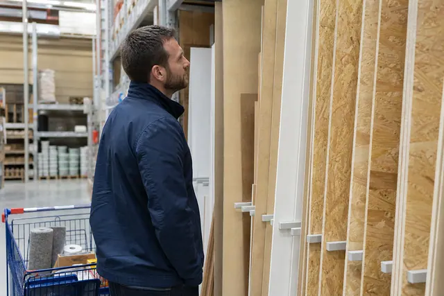 Client comparant des panneaux de bois dans un magasin de bricolage local