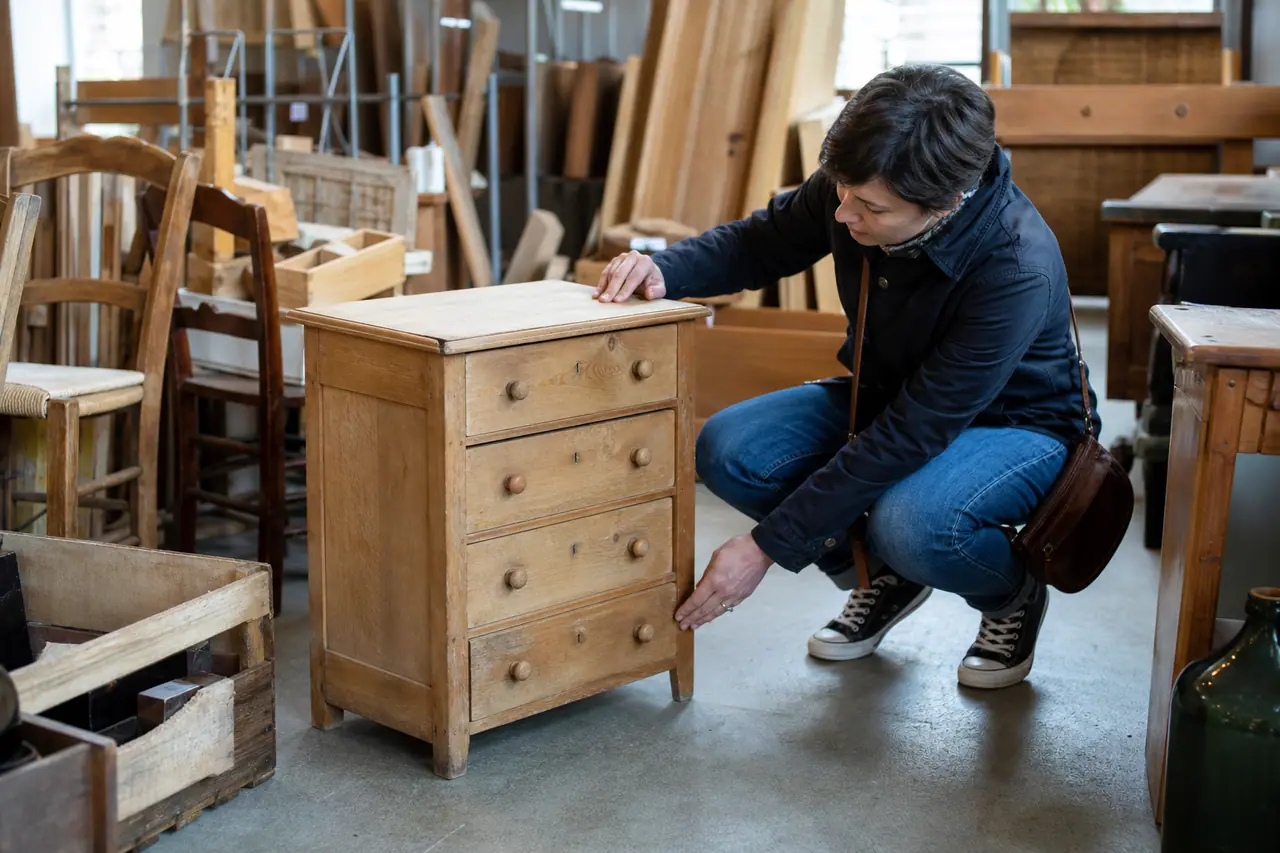 Visiteur examinant une commode en bois dans une recyclerie lumineuse.