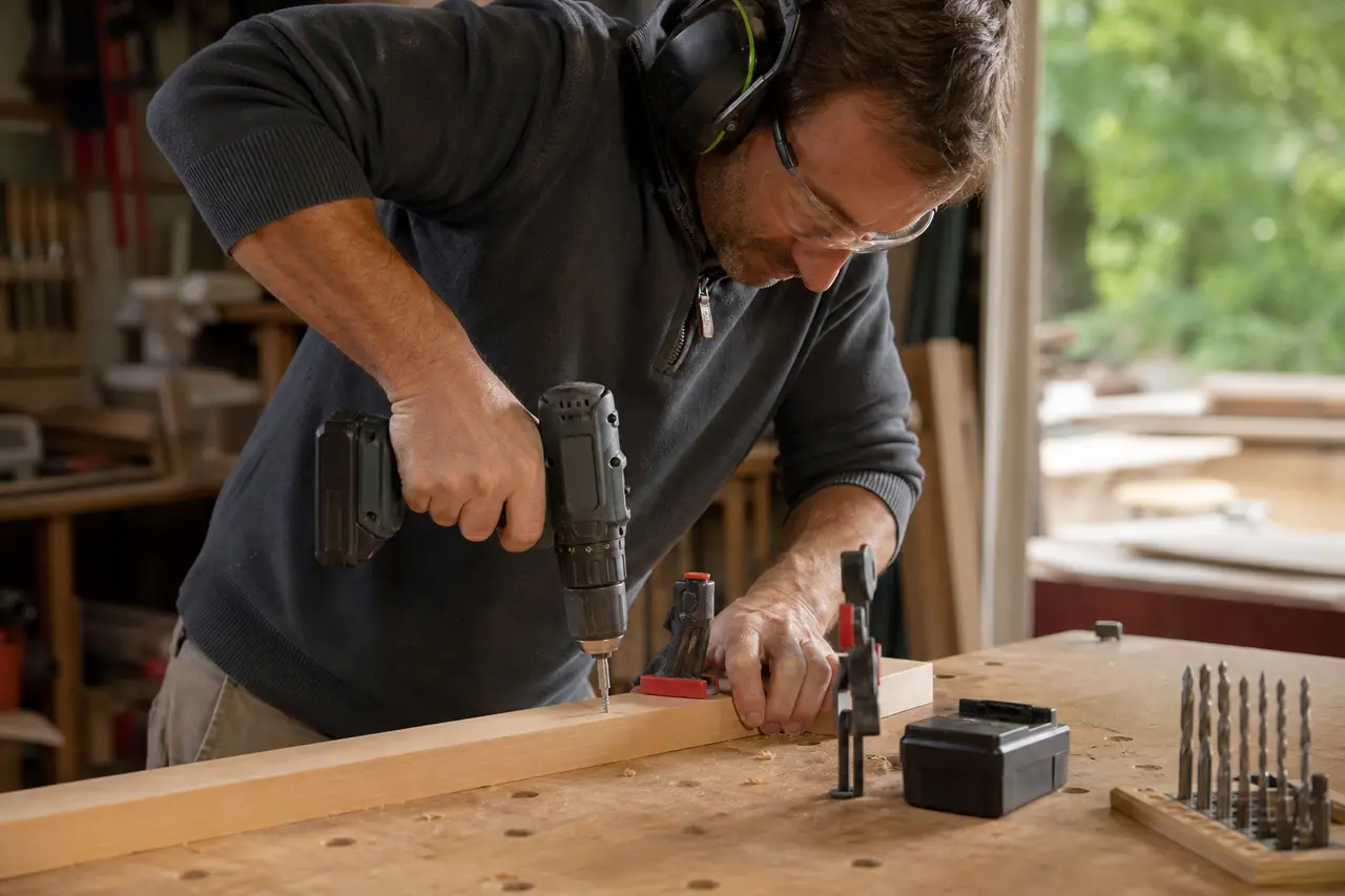 Bricoleur équipé vissant un tasseau sur établi avec une perceuse sans fil.