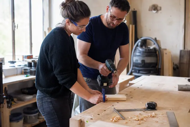 Débutante encadrée préparant une planche de bois dans un atelier partagé.