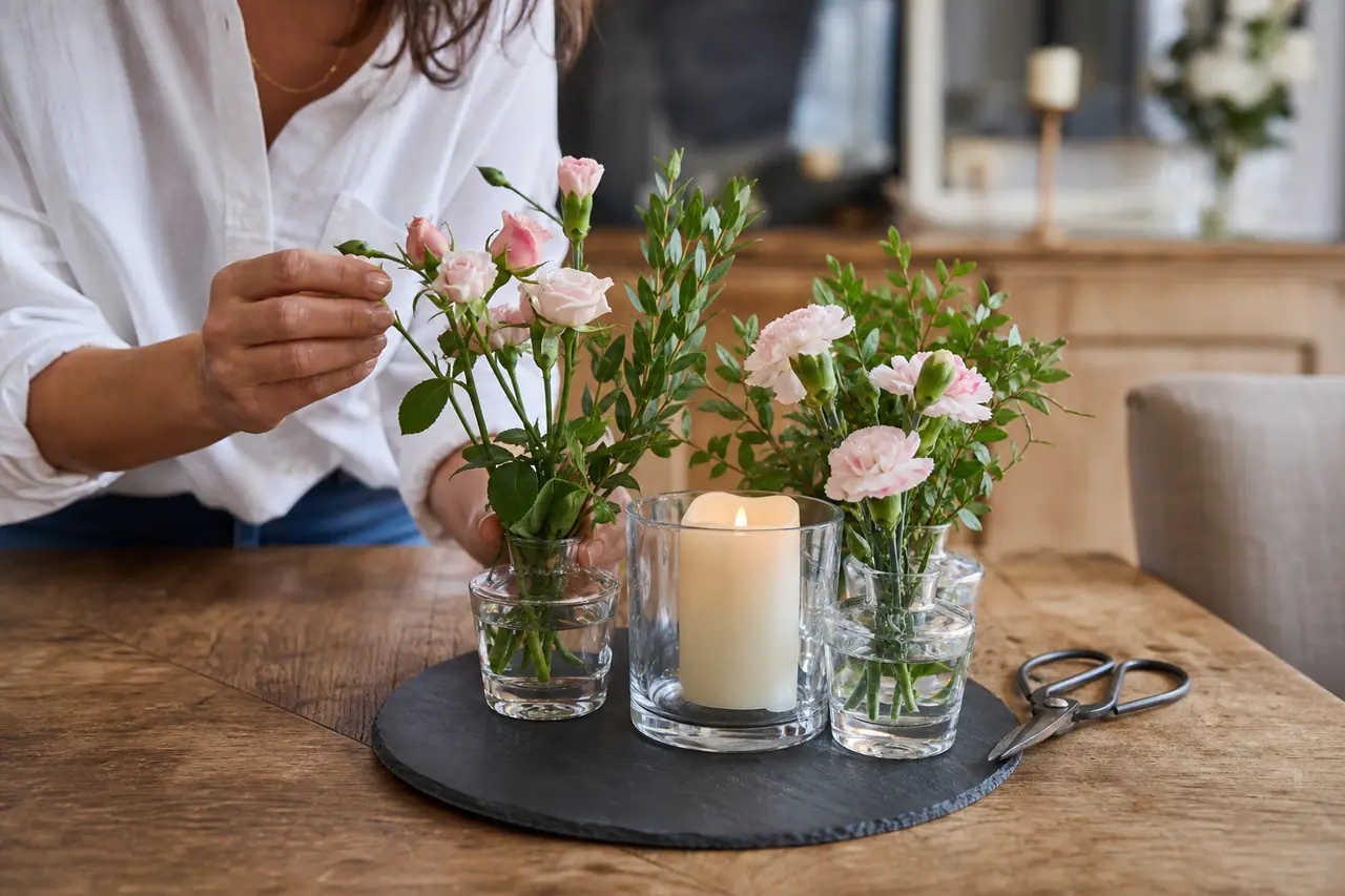 Composition florale autour d’une bougie LED sur un plateau en ardoise.