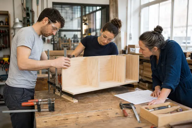 Deux voisins assemblent une étagère dans un atelier partagé lumineux et sécurisé.