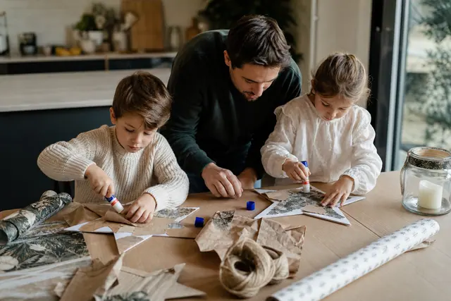 Enfants décorant des étoiles en carton et rouleaux de papier sur une table protégée.