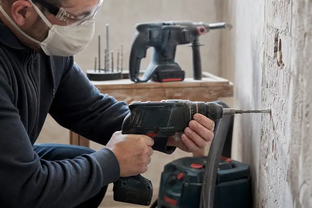 Bricoleur protégé perçant un mur en brique avec une perceuse sans fil.