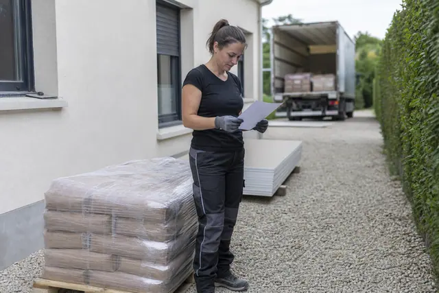 Bricoleuse vérifiant des matériaux livrés devant une maison avant leur déchargement.