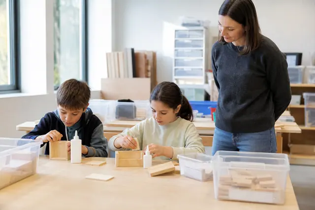Enfants assemblant une boîte en bois pré-découpée sous supervision adulte.