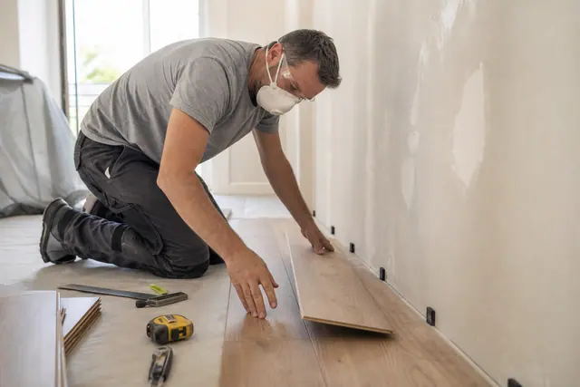 Particulier équipé posant soigneusement un sol stratifié dans une pièce en rénovation.