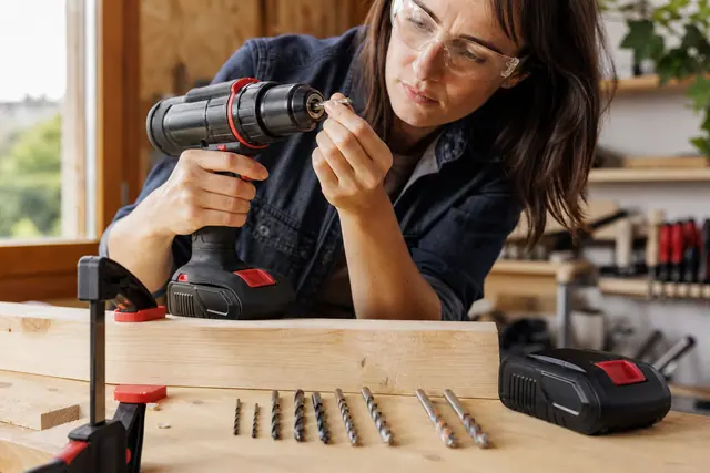 Bricoleuse réglant une perceuse sans fil avant de percer une planche serrée.