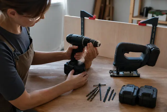 Perceuse sans fil et scie sauteuse prêtes sur un établi en bois.