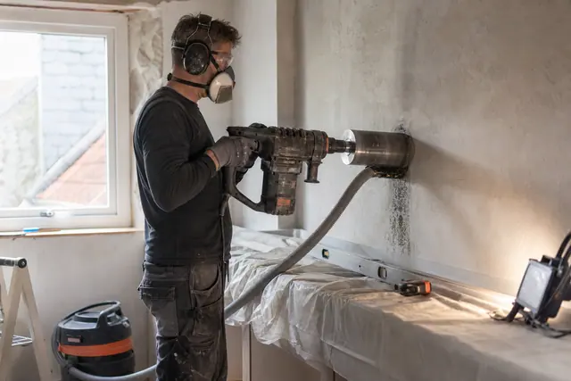 Carotteuse équipée d'une couronne diamantée perçant un mur intérieur de cuisine pour une sortie de hotte