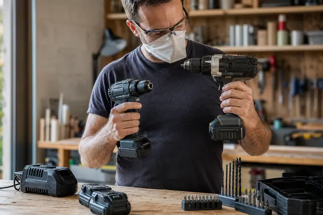 Deux perceuses-visseuses sans fil comparées sur un établi avec batteries et forets.