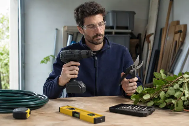 Bricoleur comparant une perceuse sans fil et un sécateur sur établi
