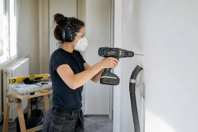 Bricoleuse équipée perçant un mur avec une perceuse sans fil