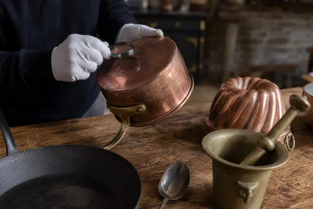Ustensiles anciens en cuivre et fonte examinés sur une table de cuisine.