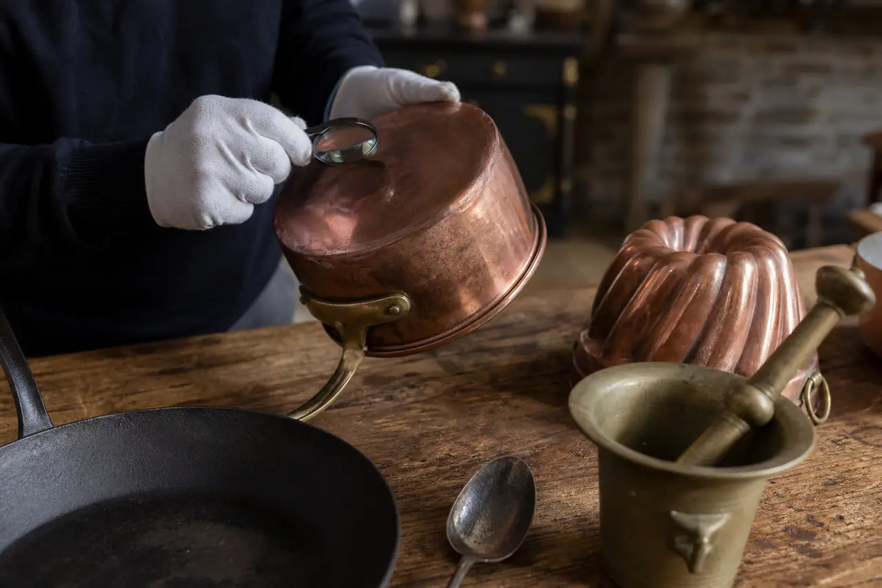 Ustensiles anciens en cuivre et fonte examinés sur une table de cuisine.