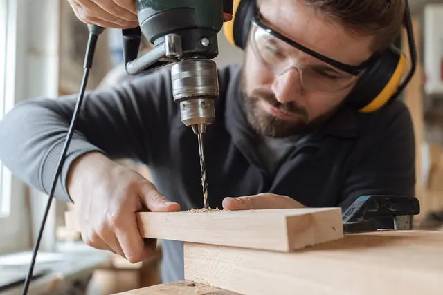 Bricoleur équipé perçant une planche de bois serrée sur un établi.