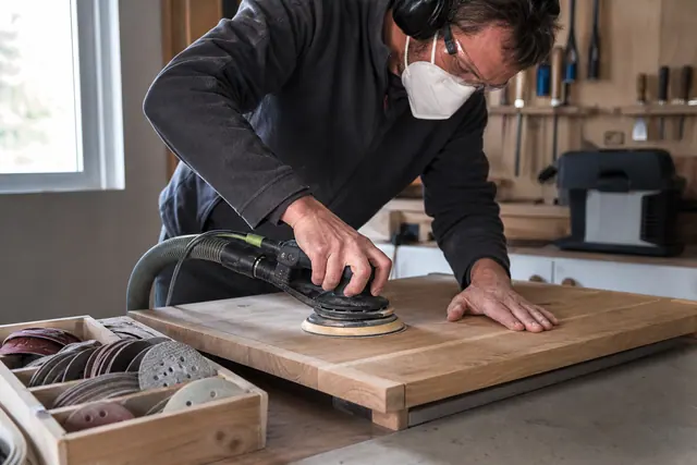 Bricoleur protégé utilisant une ponceuse excentrique sur un meuble en bois.