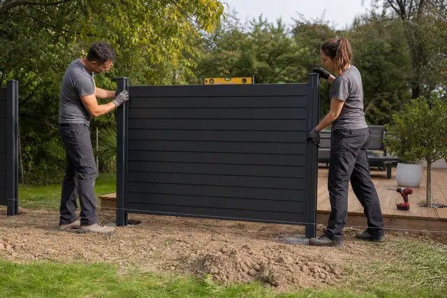Pose d’un panneau de clôture aluminium entre deux poteaux alignés dans un jardin.