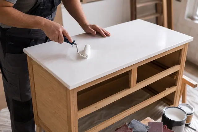 Application soignée d’une peinture brillante au rouleau sur une commode préparée.