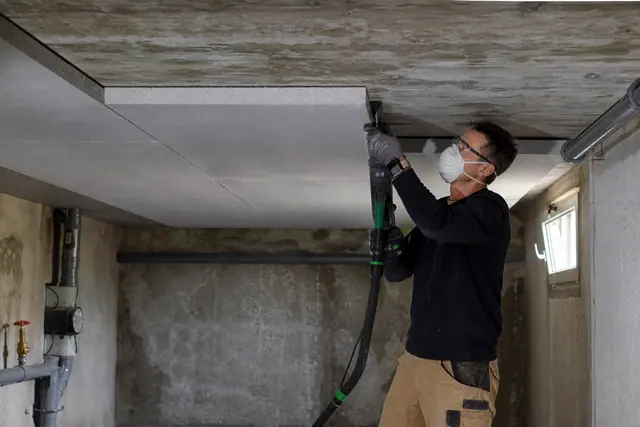 Artisan fixant des panneaux isolants sous le plafond d’une cave saine.
