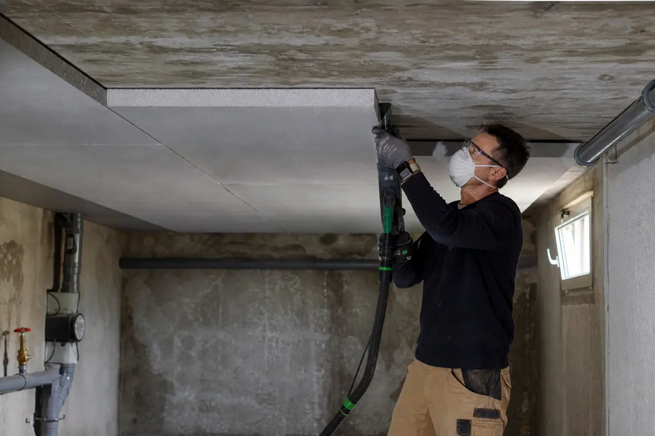 Artisan fixant des panneaux isolants sous le plafond d’une cave saine.