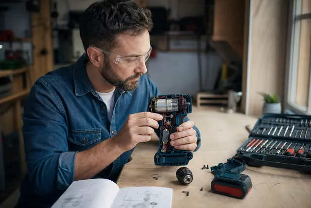 Bricoleur examinant les pièces démontées d’une perceuse sans fil sur établi.