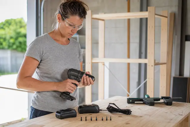 Bricoleuse préparant une visseuse sans fil et deux batteries sur un établi.