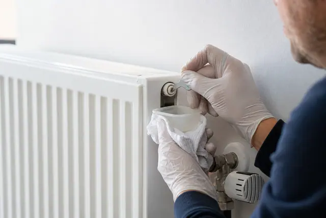 Propriétaire purgeant le purgeur supérieur d’un radiateur avec un récipient.