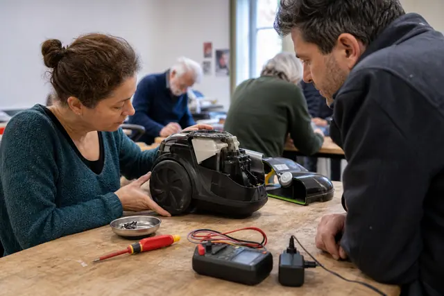 Bénévole et habitant examinent un petit appareil débranché sur un établi partagé.