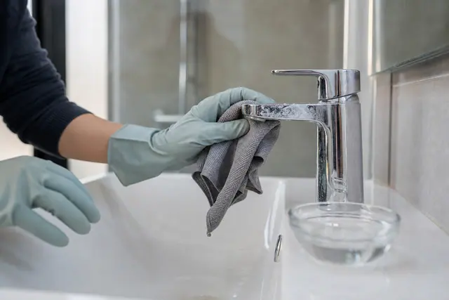 Main gantée nettoyant un robinet chromé entartré avec une microfibre douce.