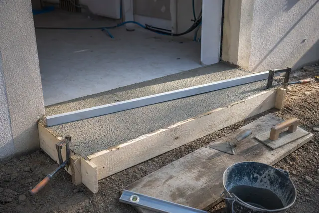 Coffrage en bois d’un seuil de porte avec béton frais tiré à la règle