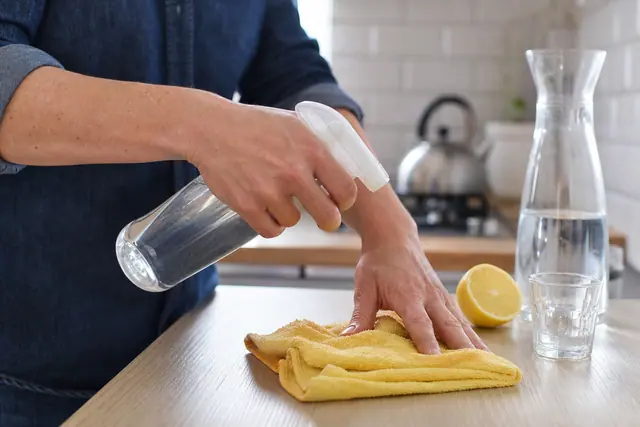 Préparation d’un spray nettoyant citronné sur chiffon microfibre dans une cuisine.
