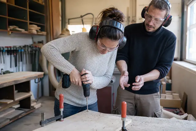 Débutante équipée perçant une planche serrée dans un atelier de bricolage.