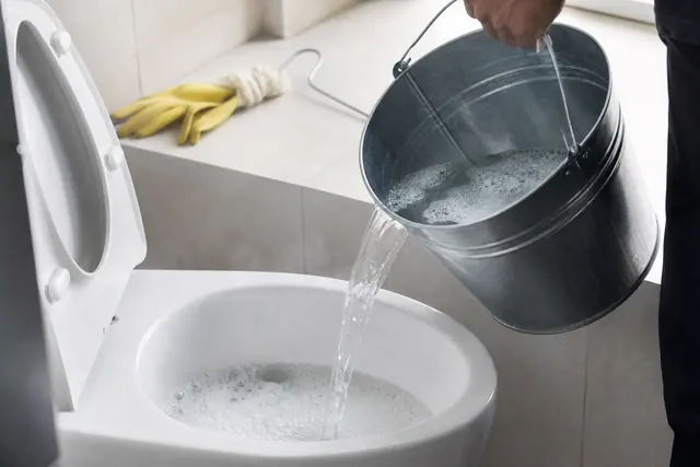 Seau d'eau chaude versé dans une cuvette de toilettes pour déboucher sans ventouse