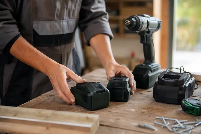 Bricoleur range deux batteries 20 V et un chargeur sur établi.