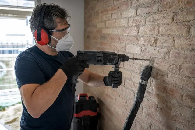 Bricoleur équipé perçant un mur de brique avec une perceuse à percussion.