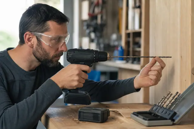 Bricoleur contrôlant le mandrin d’une perceuse-visseuse sur un établi en bois.