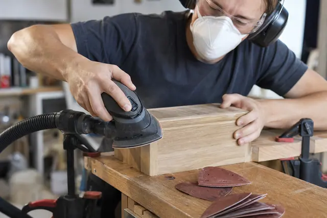 Ponceuse triangulaire utilisée avec aspiration sur l’angle d’un meuble en bois.