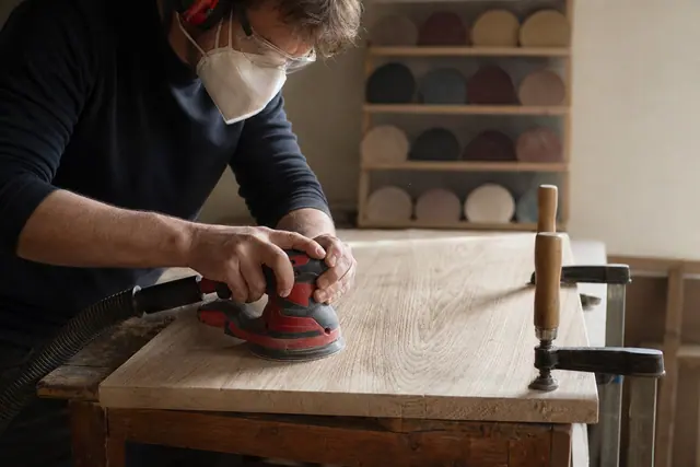 Bricoleur équipé ponçant un plateau en bois avec une ponceuse excentrique aspirée.