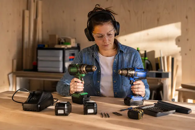 Bricoleuse comparant deux perceuses sans fil et leurs batteries sur un établi.