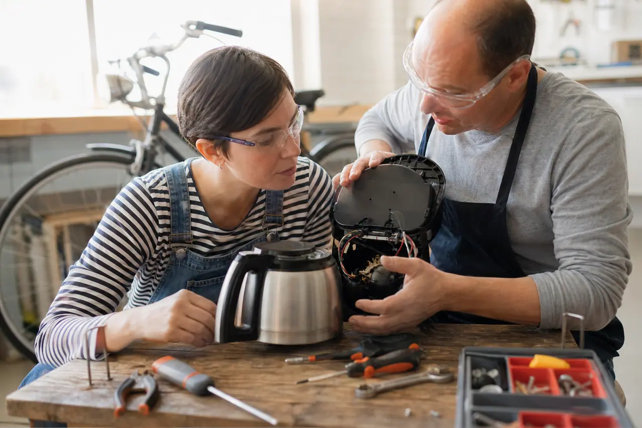 Bénévole et participante réparent une cafetière débranchée dans un atelier associatif.