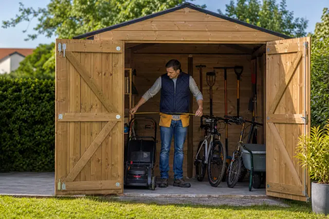 Particulier mesurant l’espace nécessaire pour une tondeuse et deux vélos dans un abri
