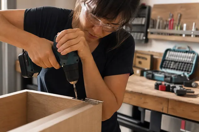 Bricoleuse équipée utilisant une visseuse compacte sur une charnière de meuble.
