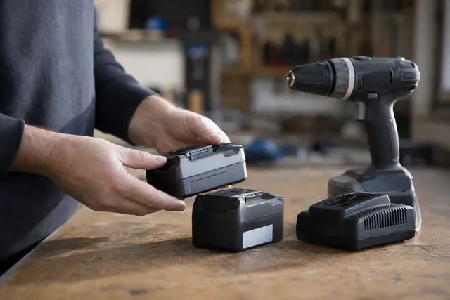 Bricoleur comparant deux batteries 18 V sur un établi d’atelier.