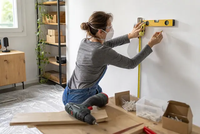 Bricoleuse traçant des repères au niveau sur un mur protégé.
