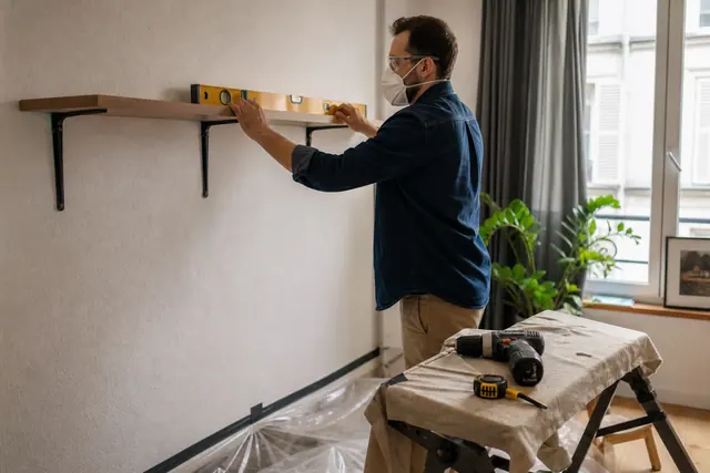 Bricoleur équipé aligne une étagère sur un mur protégé dans un salon.